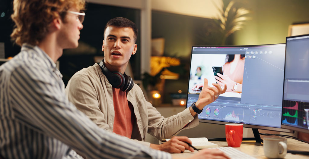 Zwei Kollegen besprechen gemeinsam ein Videoprojekt am Laptop für einheitliche Qualitätsstandards